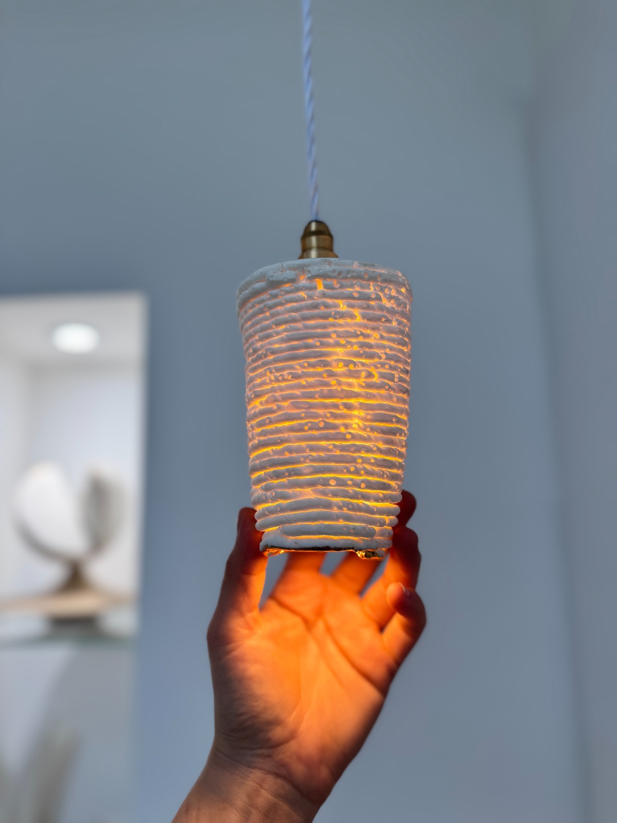 Biomaterial ceramic pendant lamp held in hand, warm amber glow