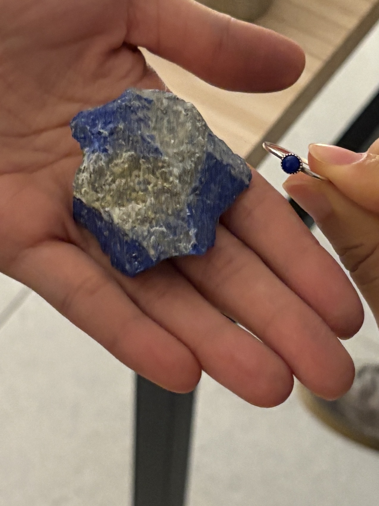 A raw lapis lazuli stone held in hand alongside a hand-set ring, from Jay Lee's material collection