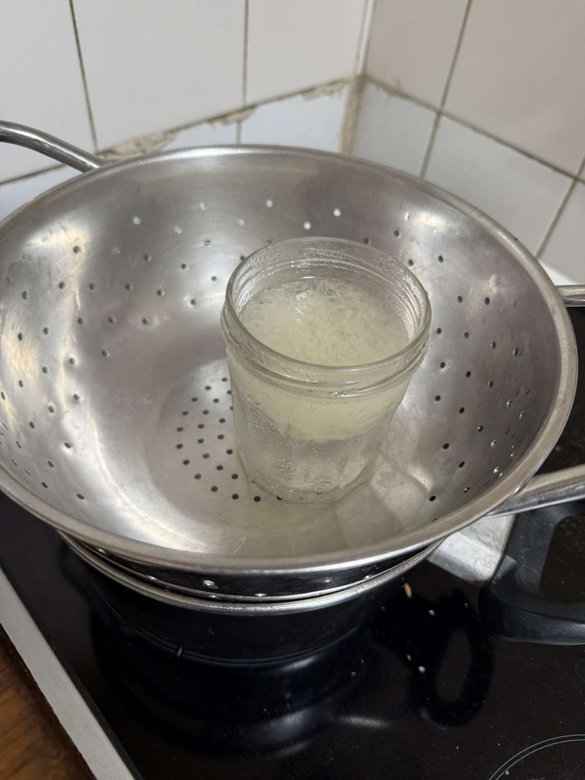A jar of extracted funori solution sitting in a colander over a double boiler pot on a stovetop